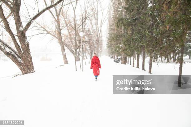 woman in outerwear walking in snowy winter park - red coat stock pictures, royalty-free photos & images