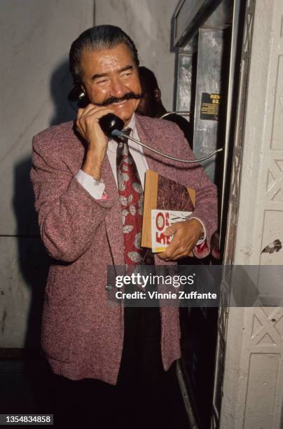 American artist LeRoy Neiman , wearing a pink blazer with a white shirt and a red tie with silver leaf motifs, using a payphone in New York City, New...