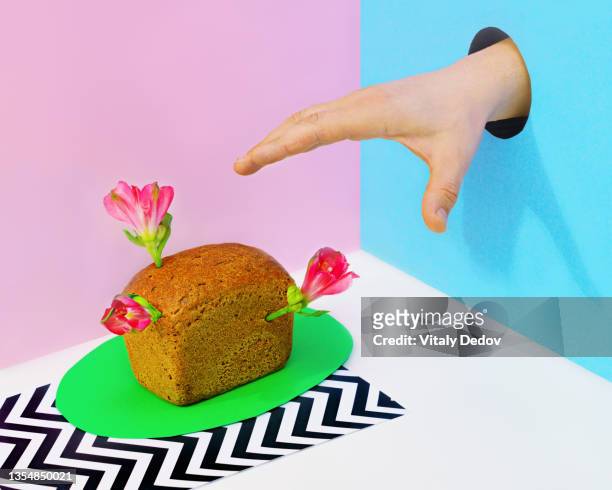 hand in hole reaching for mini loaf of bread with flowers - desire foto e immagini stock