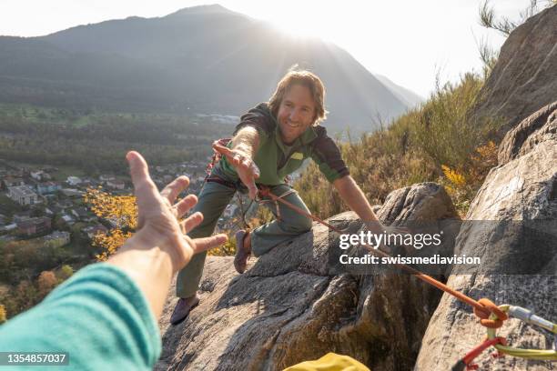pov down arm to young man climbing up a rock face - team climbing up to mountain top stockfoto's en -beelden