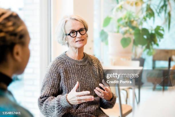 ältere frau im gespräch mit teilnehmern einer gruppentherapiesitzung - dialog stock-fotos und bilder