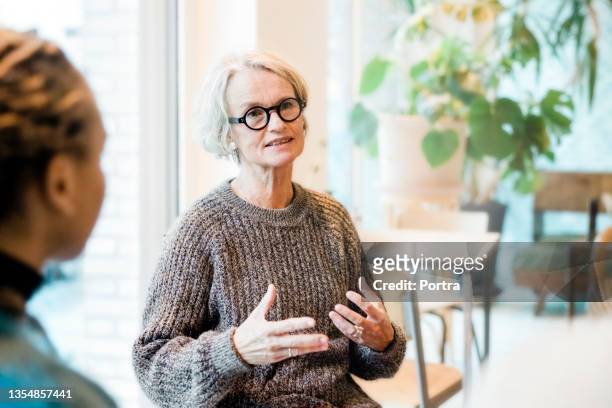 senior woman talking with participants in a group therapy session - stutten stockfoto's en -beelden