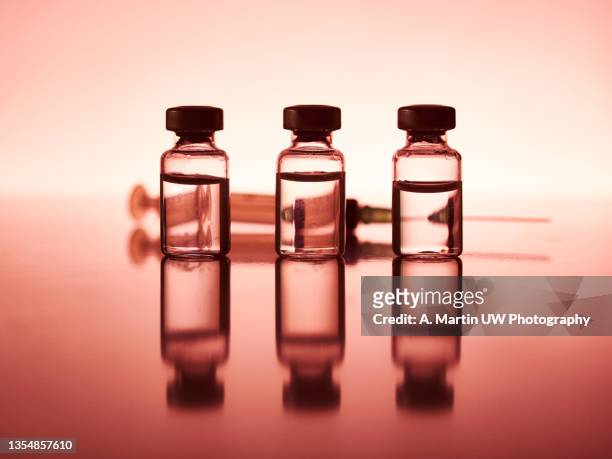 three coronavirus vaccine vials on a table with reflections and backlighting - 3 shot fotografías e imágenes de stock