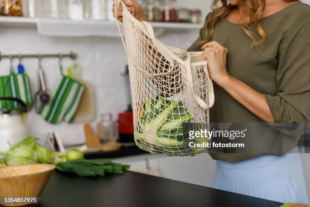 midsection of woman unpacking fresh produce from a reusable mesh bag - plant based diet stock pictures, royalty-free photos & images