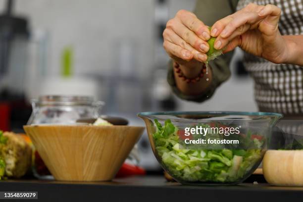 nahaufnahme einer frau, die frischen limettensaft in einen salat drückt, den sie gerade zubereitet - dressing room stock-fotos und bilder
