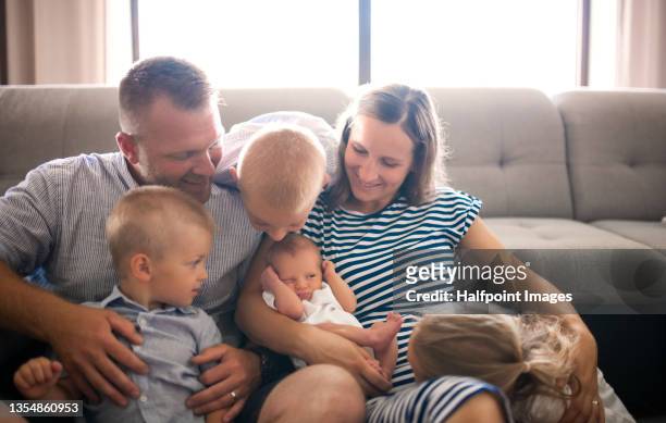 happy young family with four children sitting together on floor in living room, looking at newborn baby. - familia grande fotografías e imágenes de stock
