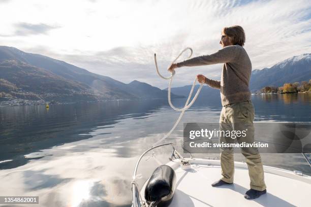 junger mann auf dem boot bereitet sich darauf vor, im herbst auf dem see zu ankern - anker stock-fotos und bilder