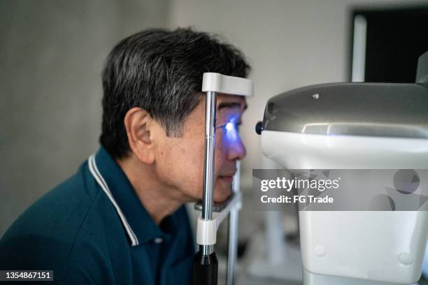 senior man doing an eye exam in a medical clinic - eye doctor stock pictures, royalty-free photos & images