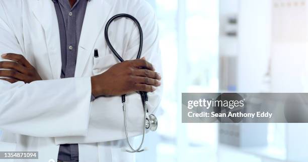 shot of an unrecognizable doctor standing with their arms crossed at a hospital - stethoscope stockfoto's en -beelden