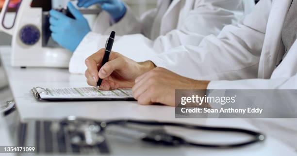 shot of an unrecognizable person writing on a form at work - medical research paper stock pictures, royalty-free photos & images