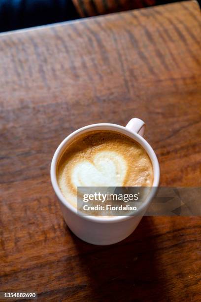 pink cup of coffee with latte art in the form of a heart standing on a wooden table - coffee frappe stock-fotos und bilder