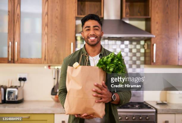 shot of a young man holding a bag of groceries - young man groceries kitchen stock pictures, royalty-free photos & images