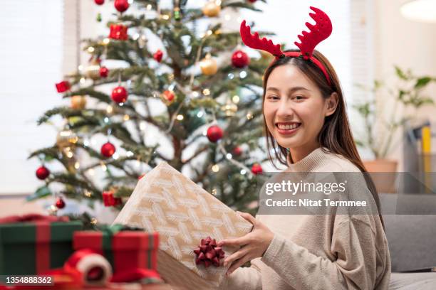 excitement young woman wearing a knitted sweater and holding christmas gifts received from her friends in an apartment. happiness during holiday and new years. - luxury lounges stock pictures, royalty-free photos & images