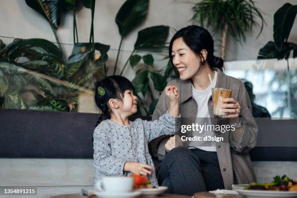 young asian mother and lovely little daughter enjoying lunch in cafe, having fun and smiling joyfully, enjoying bonding time and a happy meal together. family, food and lifestyle concept - asian family cafe stockfoto's en -beelden