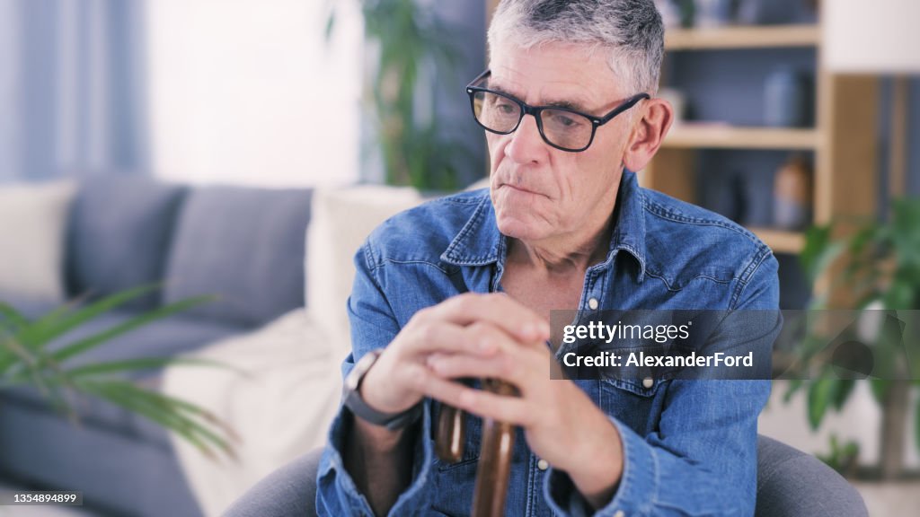 Shot of a senior man sitting on the sofa with his walking stick