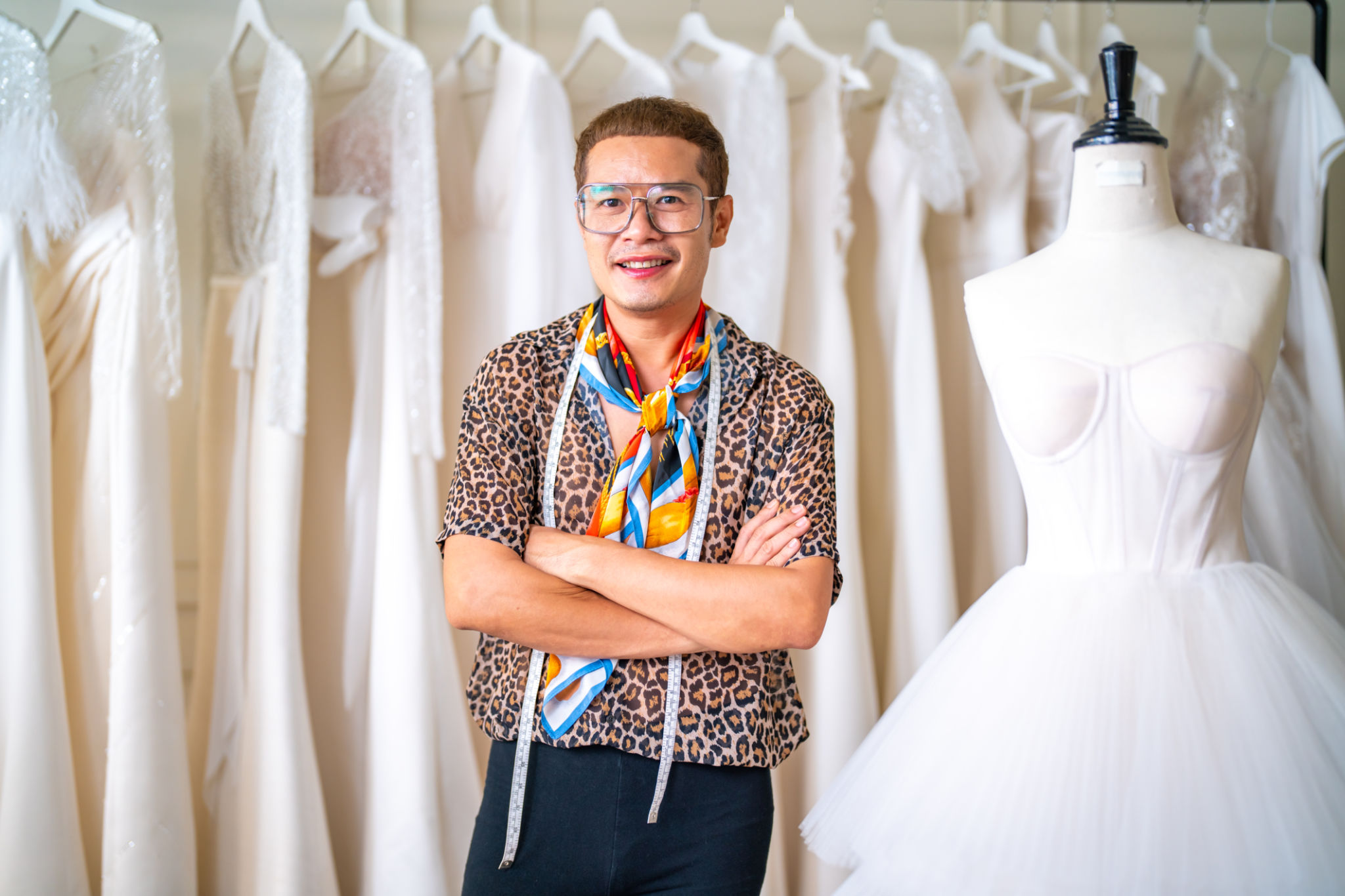 Portrait of Asian LGBTQ guy designer using tape measure measuring wedding dress on sewing mannequin Portrait of Asian LGBTQ guy designer using tape measure measuring wedding dress on sewing mannequin