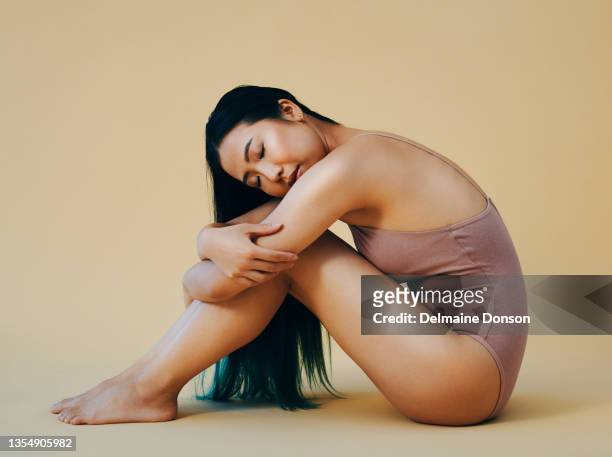 full length shot of an attractive young woman sitting alone and posing in the studio - japanese ethnicity the human body stock pictures, royalty-free photos & images