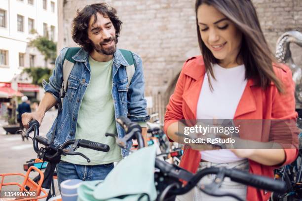 young couple on a journey using a mobile app for renting e-bikes - bike sharing stock pictures, royalty-free photos & images