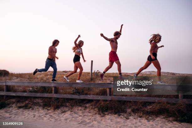 group of friends jumping and balancing on fence by beach - hossegor stockfoto's en -beelden