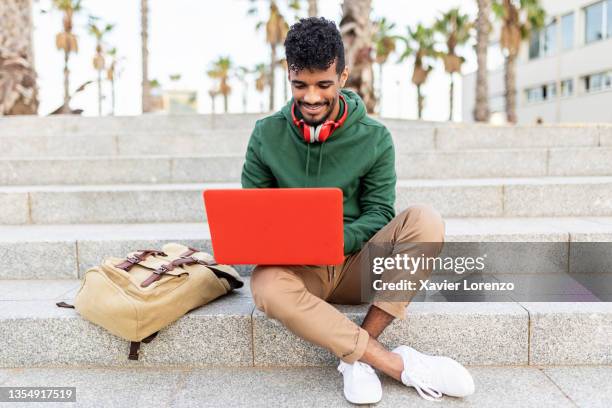 young hispanic man sitting outdoors and working on laptop - arbeiten outdoor stadt laptop stock-fotos und bilder