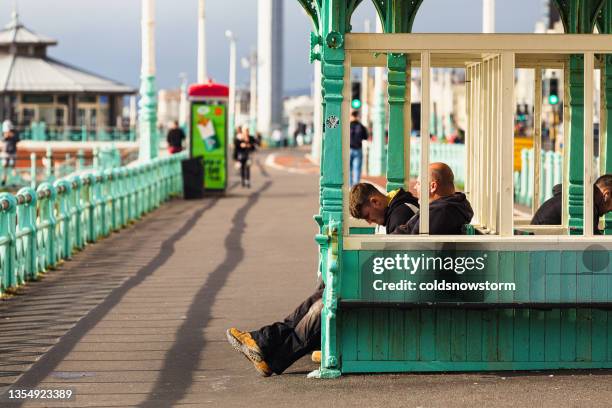 people sitting in shelter on promenade in brighton, england - windbreak stock pictures, royalty-free photos & images