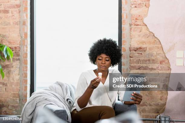 mid adult woman accesses information about medication on tablet - black pharmacist stock pictures, royalty-free photos & images