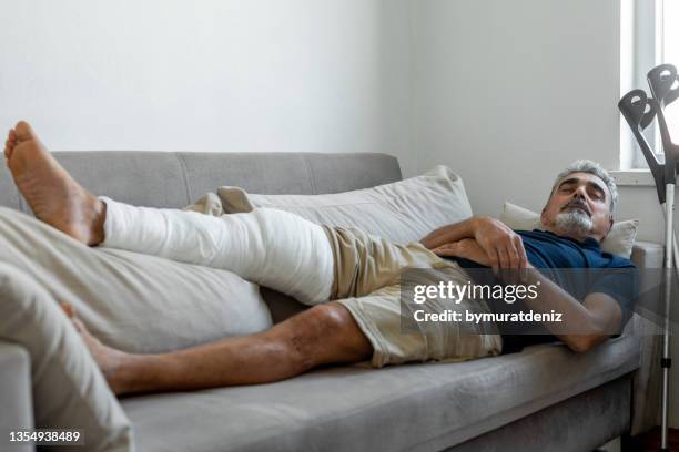 man's leg uses crutches to walk after surgery - broken leg stock pictures, royalty-free photos & images