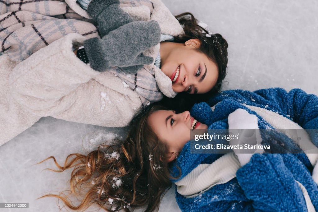 Portrait of two happy positive teenage girls friends in warm fur coats are having fun walking skating on a skating rink in the winter forest during the Christmas vacation. A couple of women in love spend time together in nature in cold winter. Top view