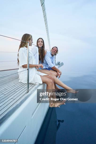 proud father sitting with his daughters on the edge of his sailboat enjoying the sunset. - family wealth stock pictures, royalty-free photos & images