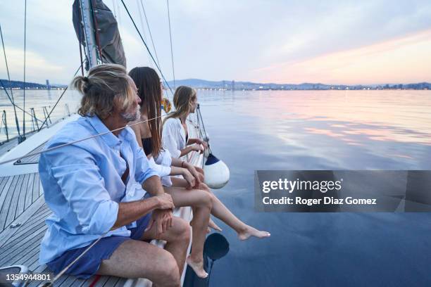 daughters and father sitting on the bow of a sailboat as they return from their weekend at sea - family wealth stock pictures, royalty-free photos & images