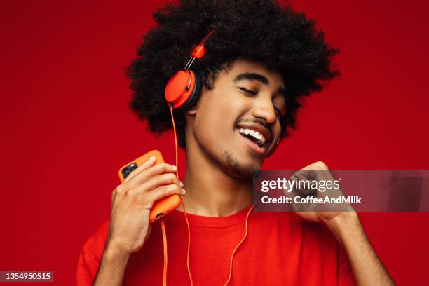 孤立した赤い背景の上に立っているアフリカの髪型を持つアフリカ系アメリカ人男性 - headphones isolated ストックフォトと画像