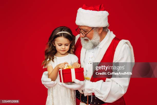 a cute little girl sitting on santa claus' lap and holding a gift - funny christmas gift stockfoto's en -beelden