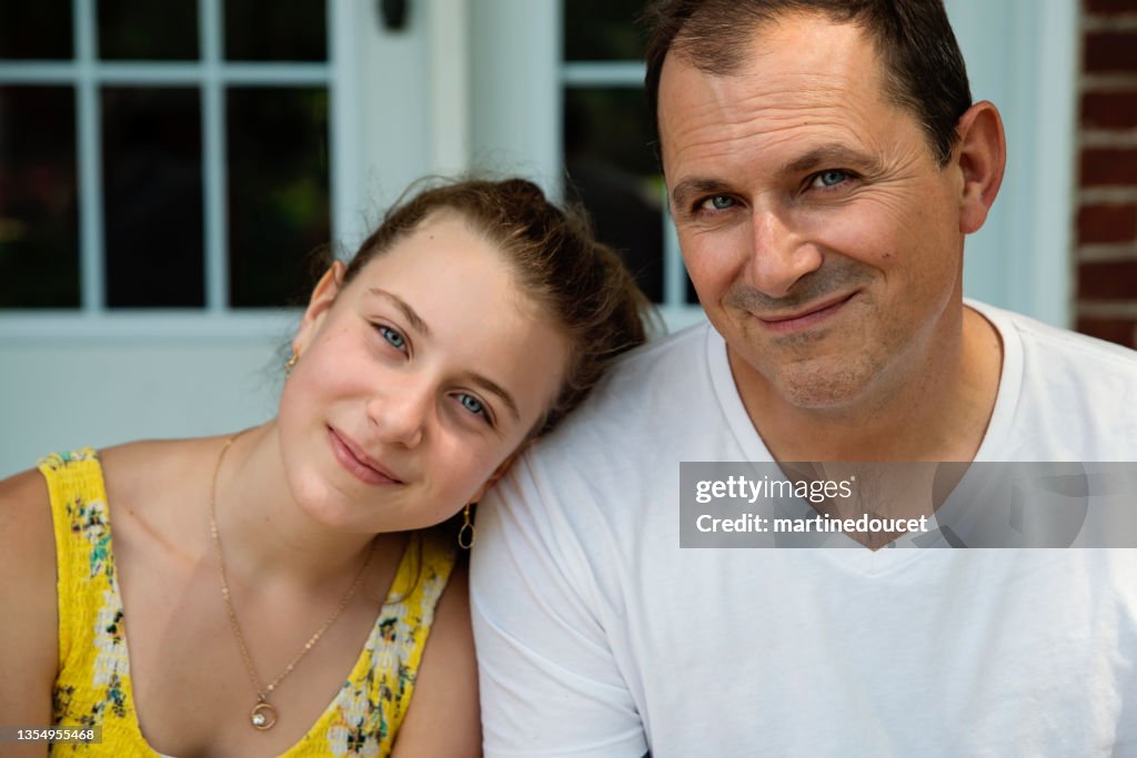 Real family portrait of father and teenage daughter on home porch in summer.