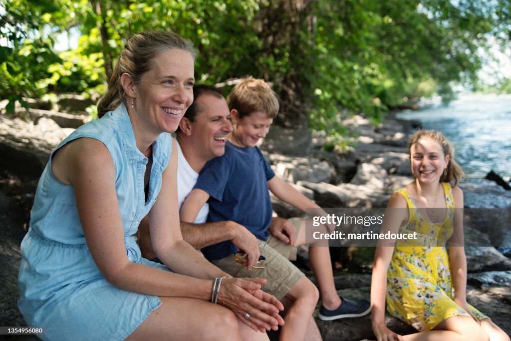 Real family portrait of 4 on riverside in summer.
