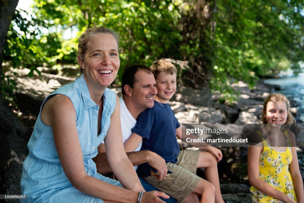 Real family portrait of 4 on riverside in summer.