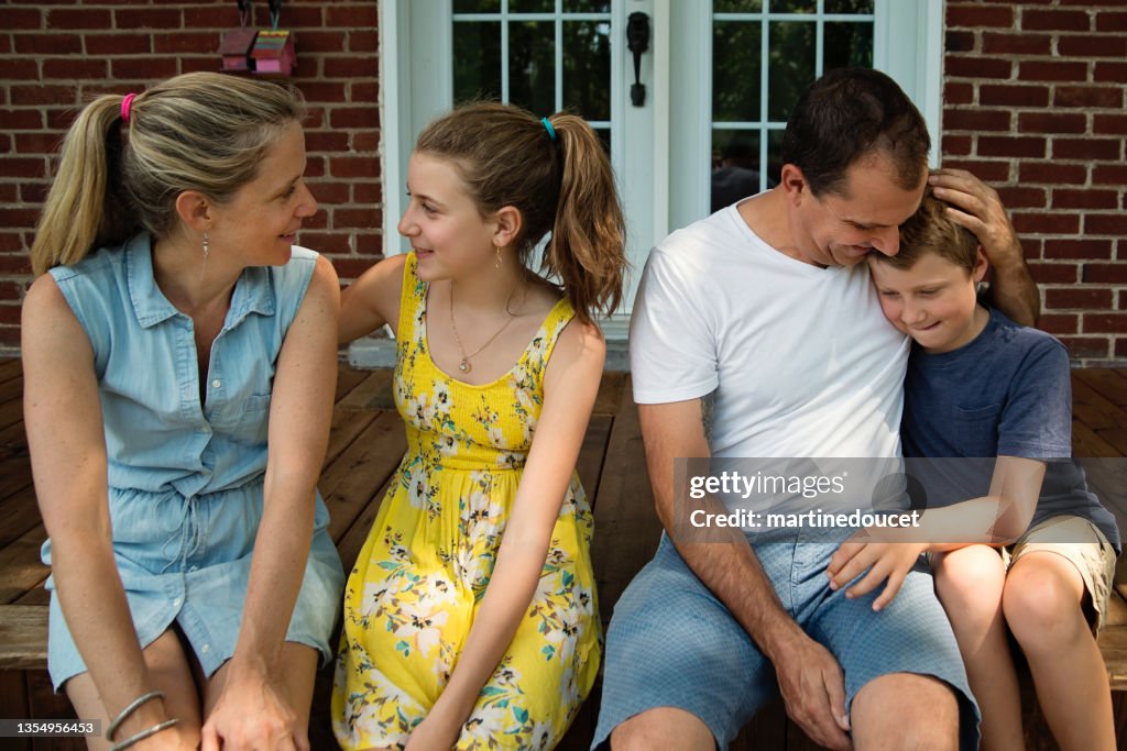 Real family portrait of 4 on home porch in summer.