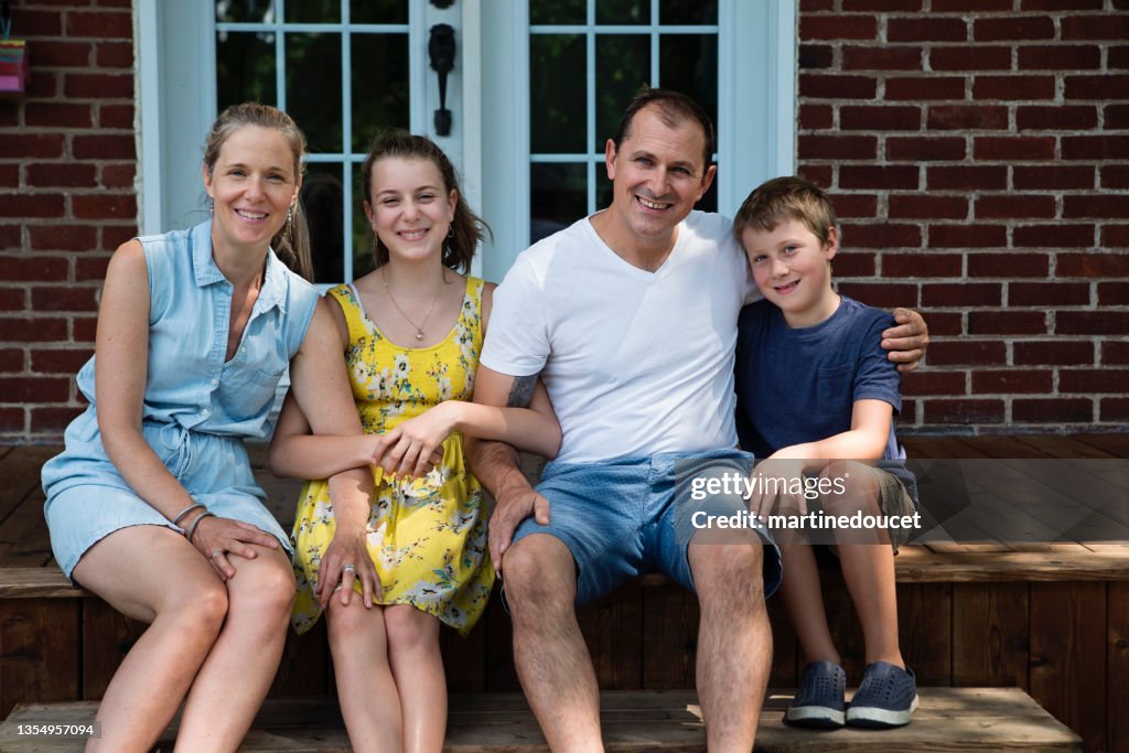Real family portrait of 4 on home porch in summer.