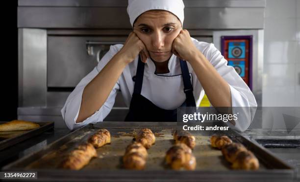 sad baker looking at some burnt bread after making a mistake with the oven - burnt stockfoto's en -beelden