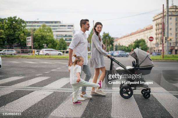 happy young family with baby in stroller and little daughter on zebra crossing outdoors in town. - ベビーカー ストックフォトと画像