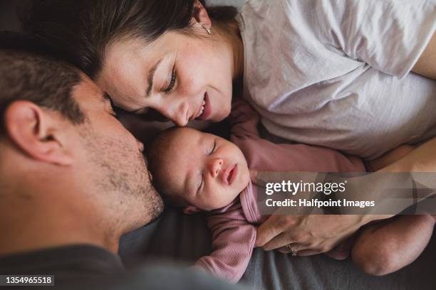 close up of young father and mother lying on bed and looking at their newborn baby at home. - pareja abrazados cama fotografías e imágenes de stock