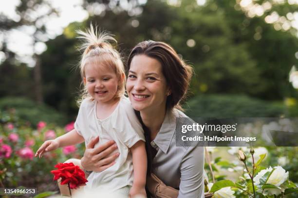 happy young mother with little daughter on walk outdoors in park, looking at camera. - white rose garden stock pictures, royalty-free photos & images