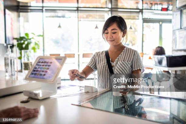 young woman using credit card reader at coffee shop counter - betalen stockfoto's en -beelden