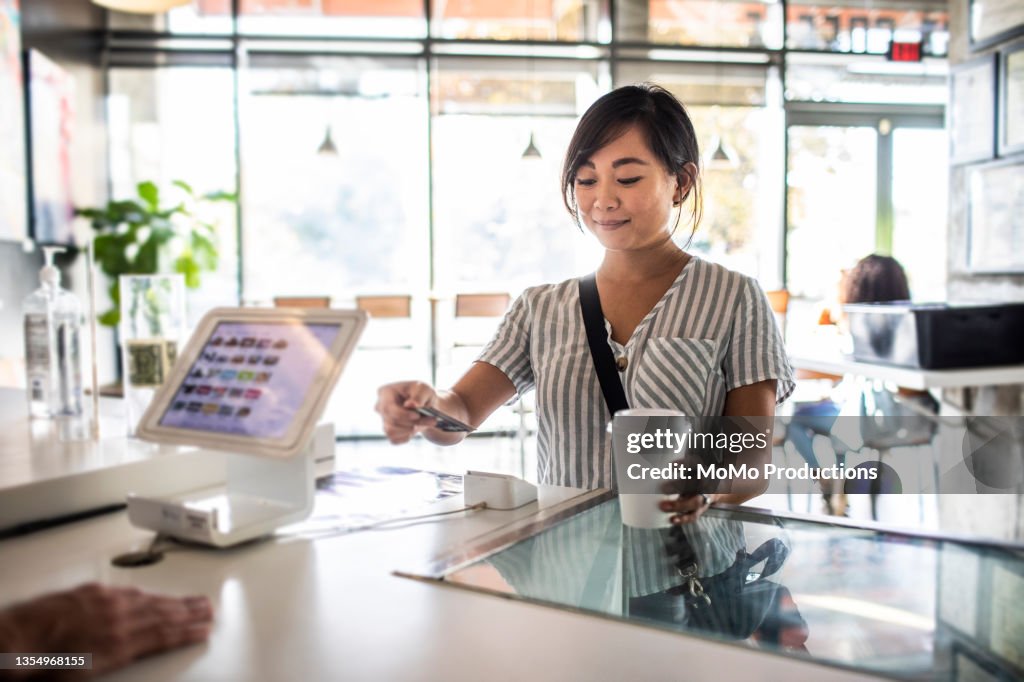 Young woman using credit card reader at coffee shop counter