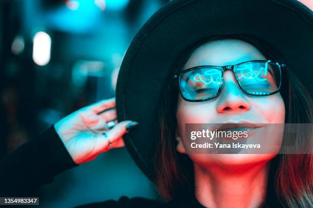 portrait of a beautiful hipster woman in glasses and hat, illuminated with neon lights - turquoise coloured stockfoto's en -beelden