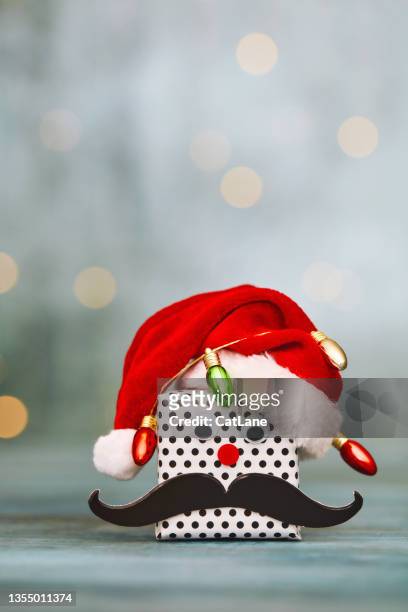 cute christmas background with christmas gift wrapped in christmas lights and wearing handlebar mustache and santa hat - claus lange stock pictures, royalty-free photos & images