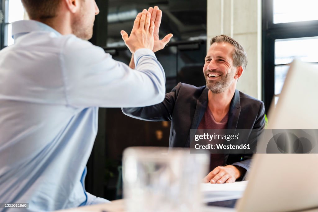 Happy businessman giving high-five to coworker in meeting