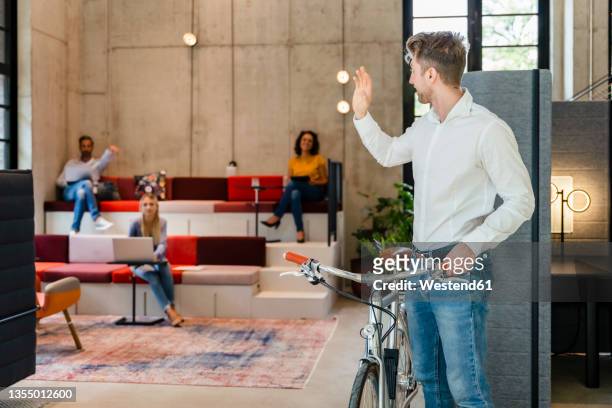 businessman with bicycle waving hand to colleagues in office - businessman after work stock-fotos und bilder