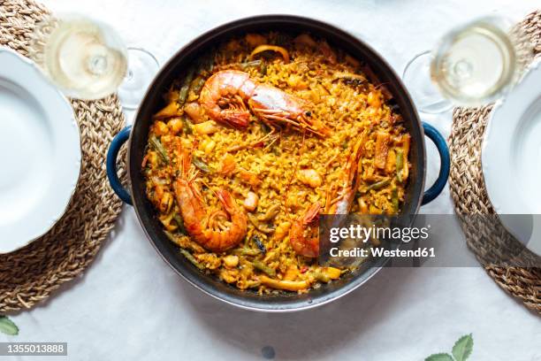 pan of ready-to-eat paella with shrimps and two glasses of white wine - paella stock-fotos und bilder