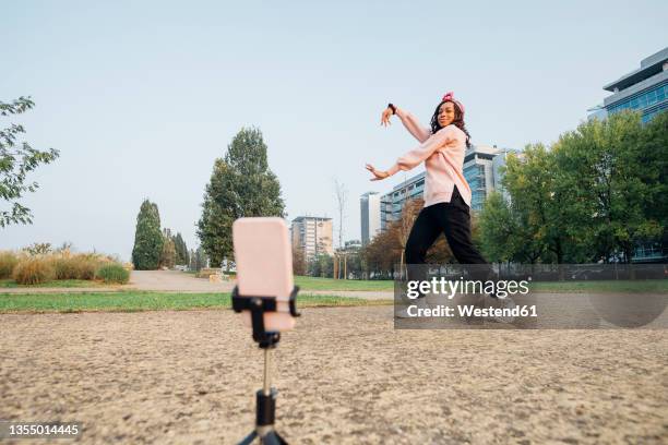 woman filming dance on mobile phone at park - tripod stock-fotos und bilder