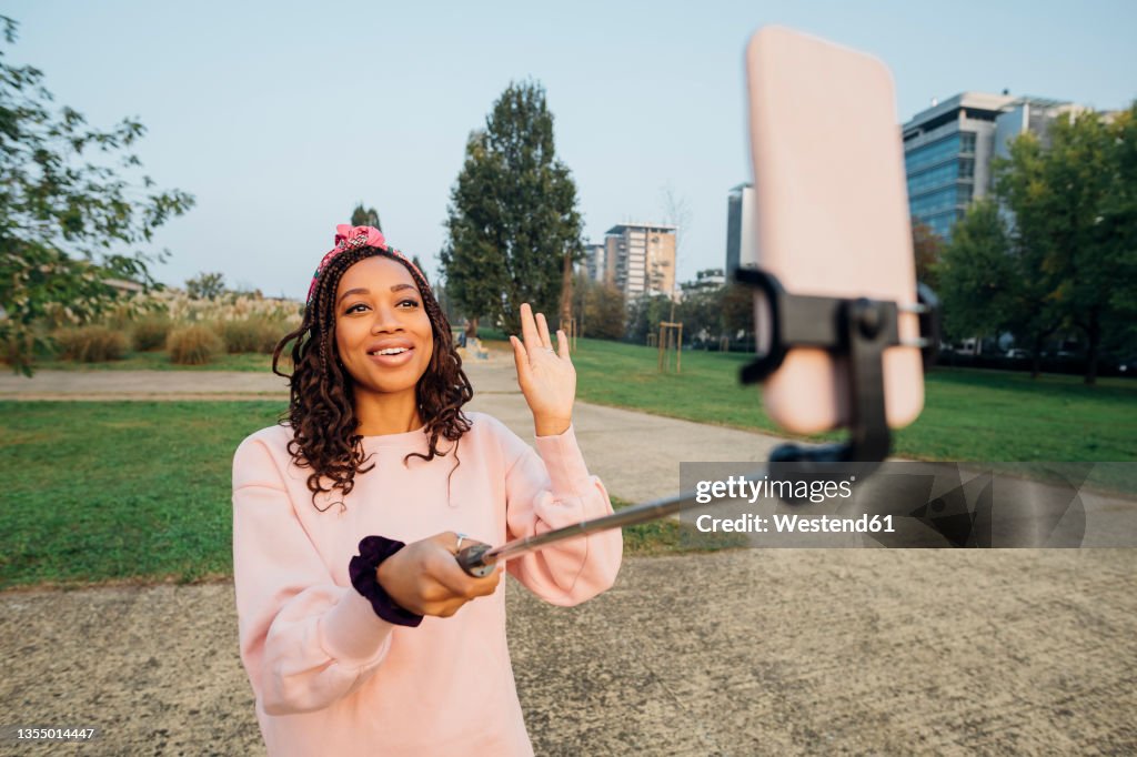 Woman waving hand while vlogging through smart phone at park